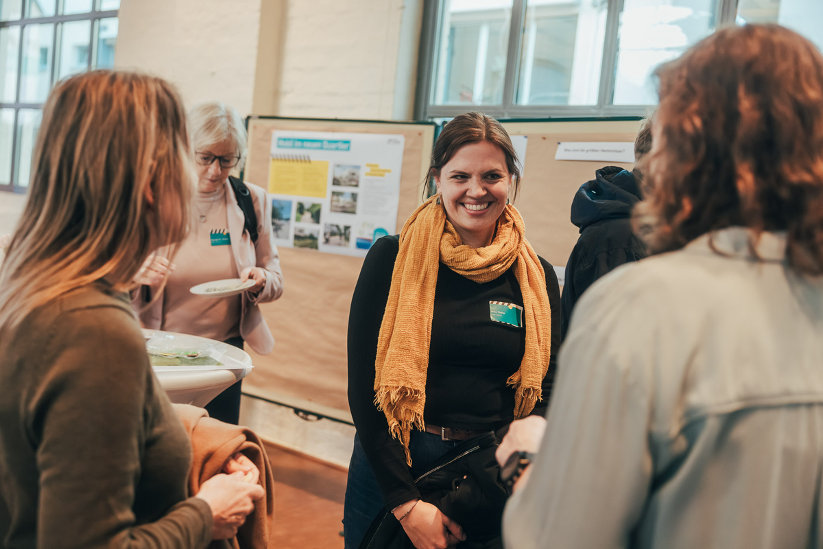 Mehrere Teilnehmende unterhalten sich vor Ausstellungstafeln im Foyer des Mobilnetzwerktreffens 2025.